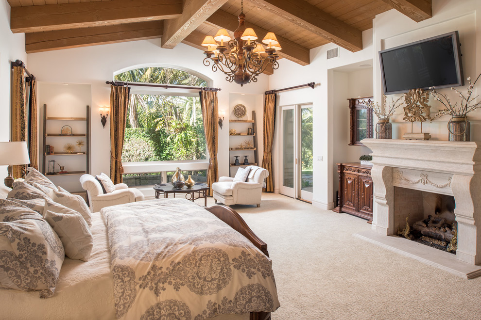 Photo of a mediterranean master bedroom in San Diego with white walls, carpet, a standard fireplace and beige floor.