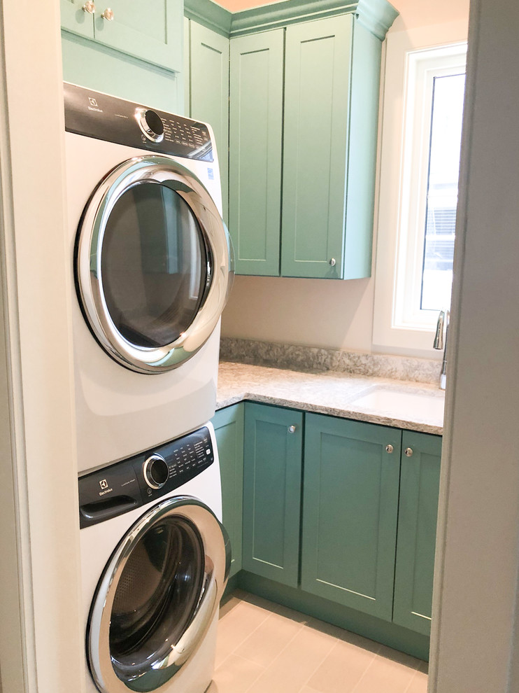 This is an example of a mid-sized traditional galley dedicated laundry room in Tampa with an undermount sink, shaker cabinets, blue cabinets, marble benchtops, beige walls, ceramic floors, a stacked washer and dryer, beige floor and grey benchtop.