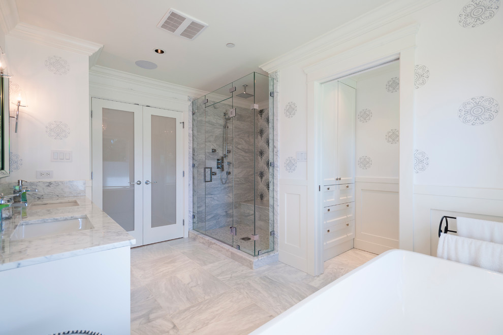 Photo of a large transitional master bathroom in Vancouver with an undermount sink, shaker cabinets, white cabinets, marble benchtops, a freestanding tub, an alcove shower, a one-piece toilet, white tile, porcelain tile, white walls and marble floors.