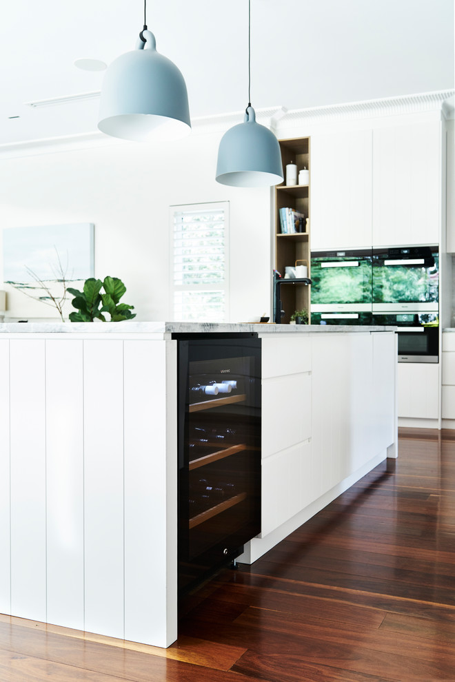 Large scandinavian l-shaped open plan kitchen in Sydney with an undermount sink, flat-panel cabinets, white cabinets, marble benchtops, white splashback, stone slab splashback, stainless steel appliances, medium hardwood floors, with island and brown floor.
