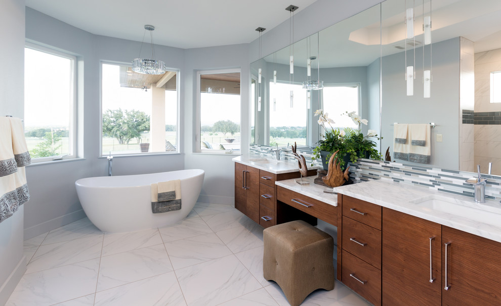 Large contemporary bathroom in Austin with an undermount sink, flat-panel cabinets, medium wood cabinets, marble benchtops, a freestanding tub, white tile, blue walls and porcelain floors.