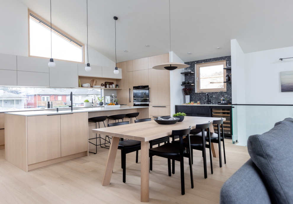 Design ideas for a mid-sized scandinavian u-shaped eat-in kitchen in Vancouver with a drop-in sink, flat-panel cabinets, light wood cabinets, black appliances, light hardwood floors, with island, beige floor and grey benchtop.
