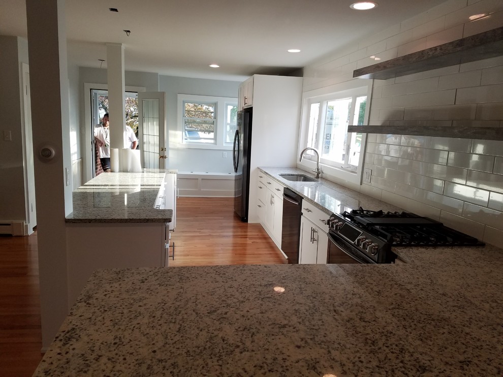 Mid-sized transitional l-shaped medium tone wood floor and brown floor open concept kitchen photo with an undermount sink, recessed-panel cabinets, white cabinets, granite countertops, white backsplash, subway tile backsplash, black appliances, an island and beige countertops