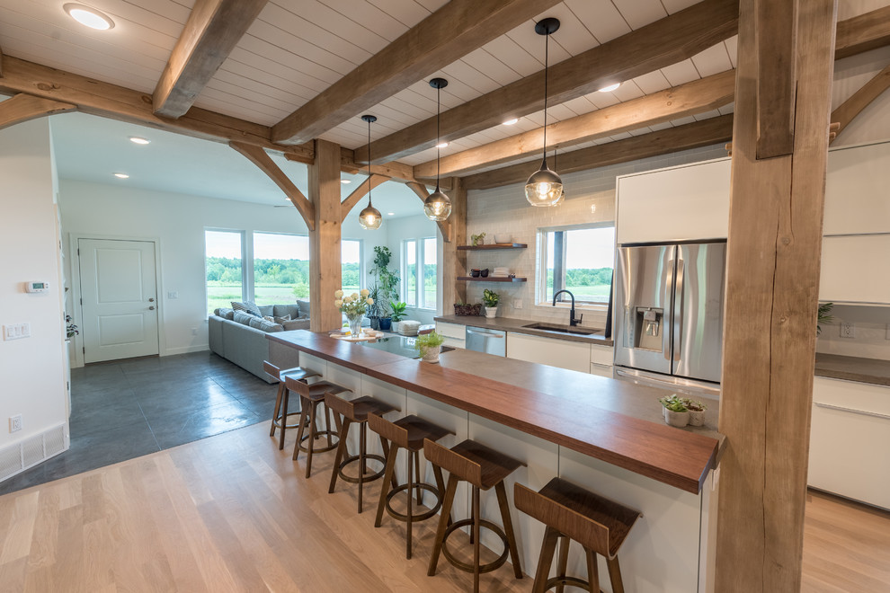 Mid-sized country single-wall open plan kitchen in Minneapolis with an undermount sink, flat-panel cabinets, white cabinets, concrete benchtops, white splashback, subway tile splashback, stainless steel appliances, medium hardwood floors, with island, brown floor and grey benchtop.