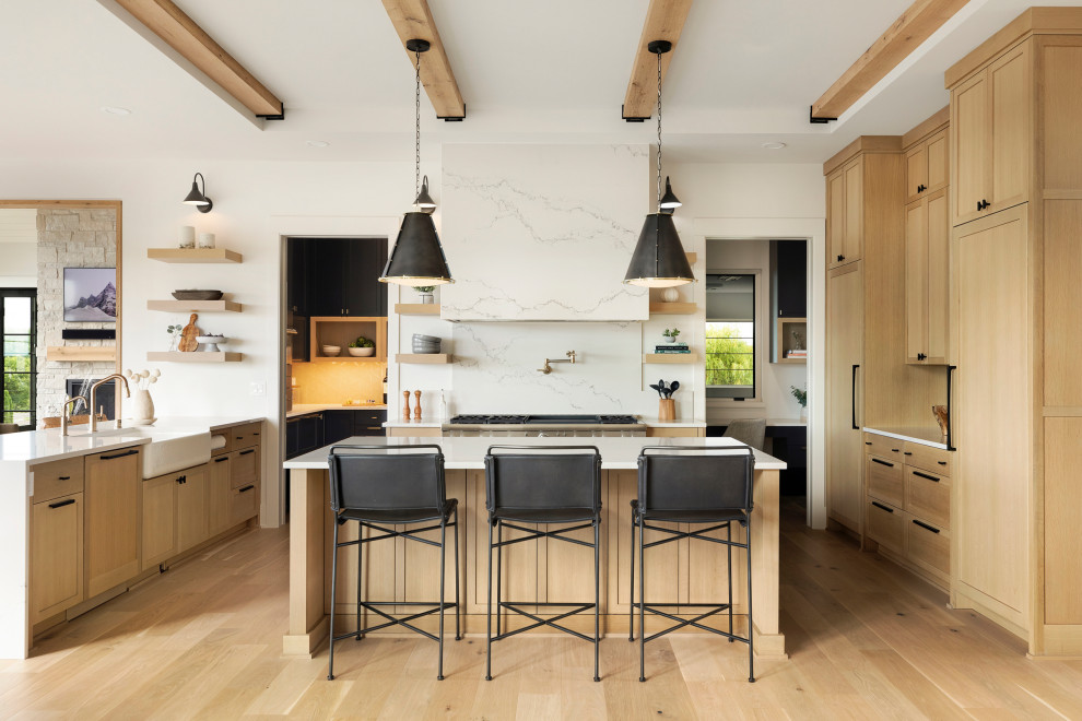 Classic u-shaped kitchen in Minneapolis with a submerged sink, light wood cabinets, engineered stone countertops, white splashback, engineered quartz splashback, stainless steel appliances, light hardwood flooring, an island, white worktops, a vaulted ceiling, shaker cabinets and brown floors.