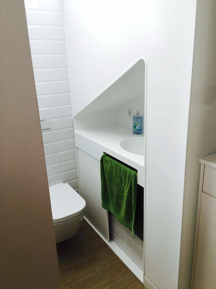 Small contemporary powder room in Valencia with a one-piece toilet, white tile, ceramic tile, white walls, an integrated sink and solid surface benchtops.