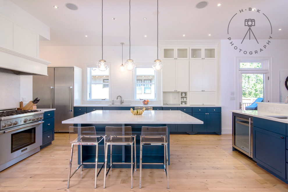 Open concept kitchen - large transitional u-shaped light wood floor and beige floor open concept kitchen idea with a drop-in sink, recessed-panel cabinets, blue cabinets, white backsplash, stainless steel appliances, two islands and white countertops