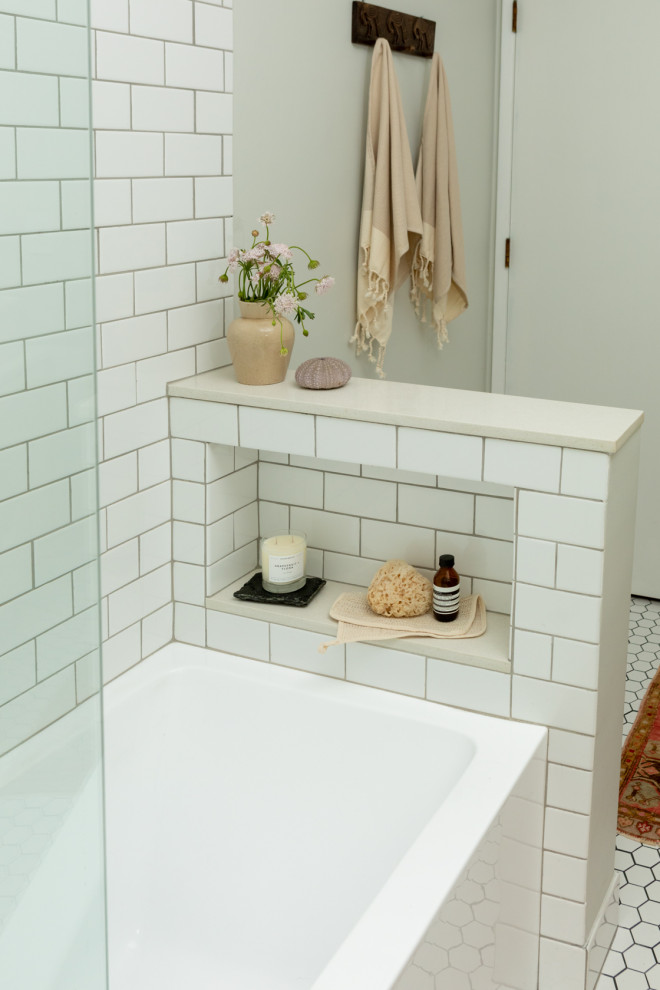 Источник вдохновения для домашнего уюта: маленькая ванная комната в стиле ретро с плоскими фасадами, светлыми деревянными фасадами, ванной в нише, душем над ванной, унитазом-моноблоком, белой плиткой, керамической плиткой, серыми стенами, полом из керамогранита, настольной раковиной, столешницей из искусственного кварца, белым полом, душем с распашными дверями, белой столешницей, нишей, тумбой под одну раковину и напольной тумбой для на участке и в саду