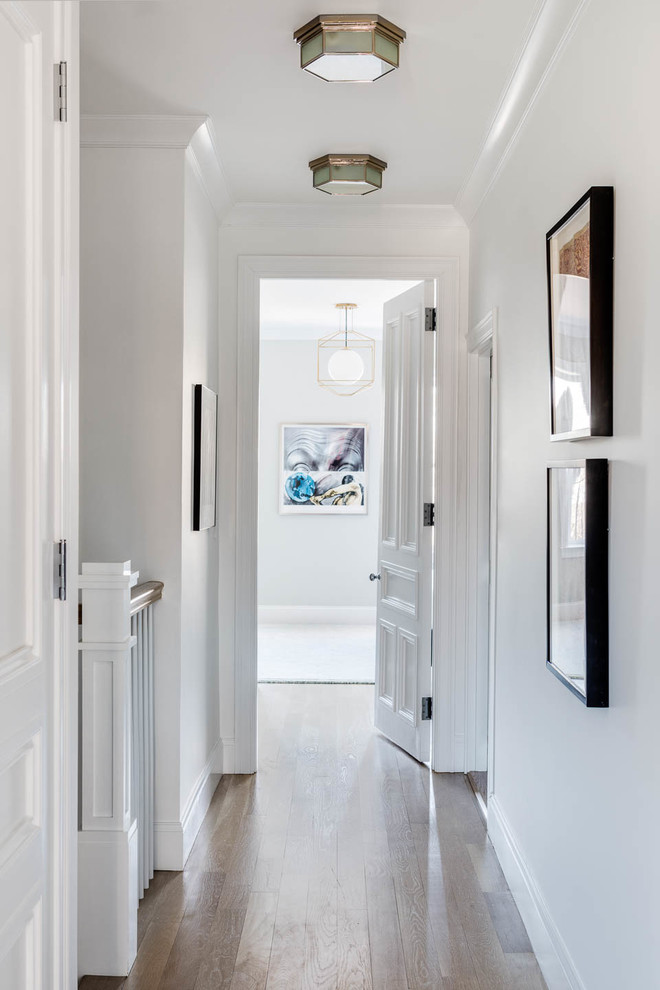 This is an example of a transitional hallway in Boston with white walls and medium hardwood floors.