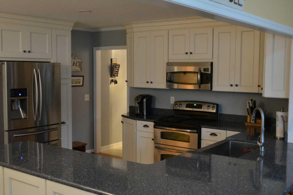 Mid-sized transitional u-shaped dark wood floor and brown floor eat-in kitchen photo with a farmhouse sink, shaker cabinets, beige cabinets, granite countertops, gray backsplash, mosaic tile backsplash, stainless steel appliances, a peninsula and black countertops