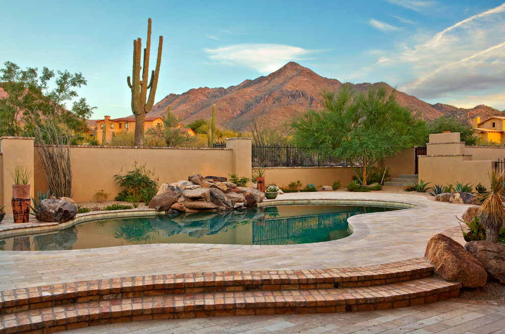 This is an example of a large mediterranean backyard custom-shaped pool in Phoenix with brick pavers and a water feature.