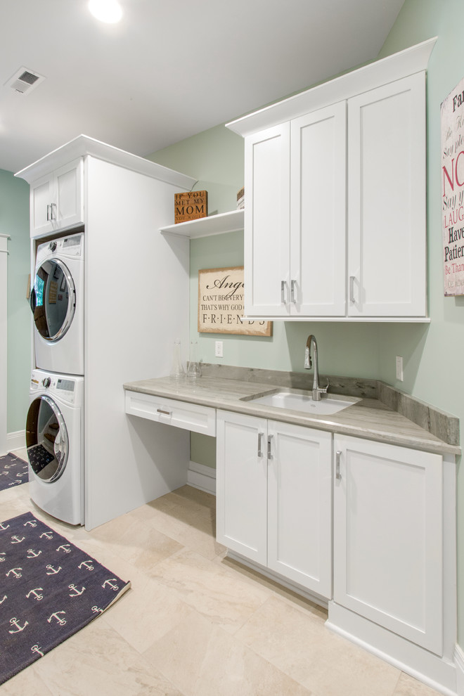 Inspiration for a mid-sized beach style galley utility room in Milwaukee with an undermount sink, shaker cabinets, white cabinets, granite benchtops, green walls, travertine floors and a stacked washer and dryer.
