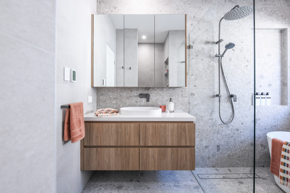 Photo of a medium sized contemporary family bathroom in Sydney with light wood cabinets, a freestanding bath, a walk-in shower, grey tiles, multi-coloured tiles, ceramic flooring, a vessel sink, engineered stone worktops, grey floors, an open shower, white worktops, a wall niche, a single sink and a floating vanity unit.