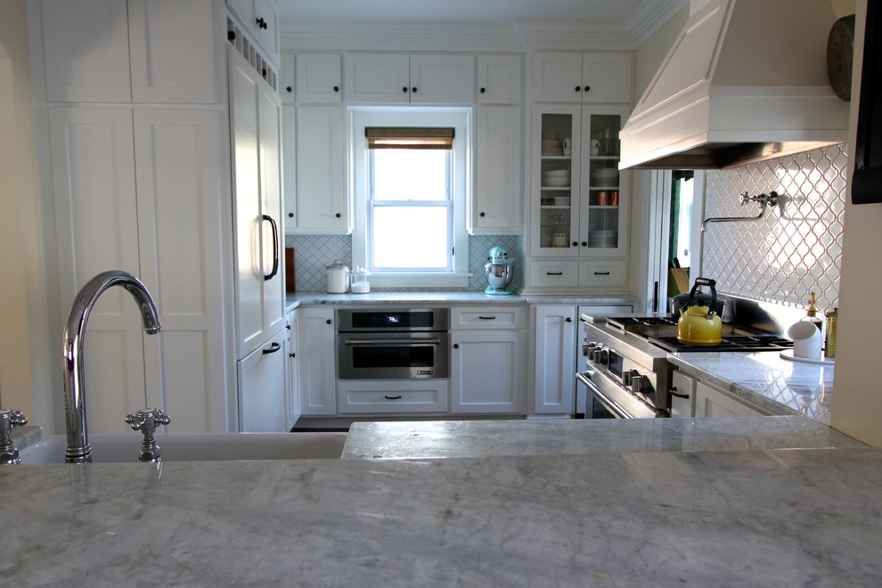 Example of a transitional medium tone wood floor kitchen design in Omaha with a farmhouse sink, shaker cabinets, white cabinets, quartzite countertops, white backsplash, ceramic backsplash, stainless steel appliances and a peninsula