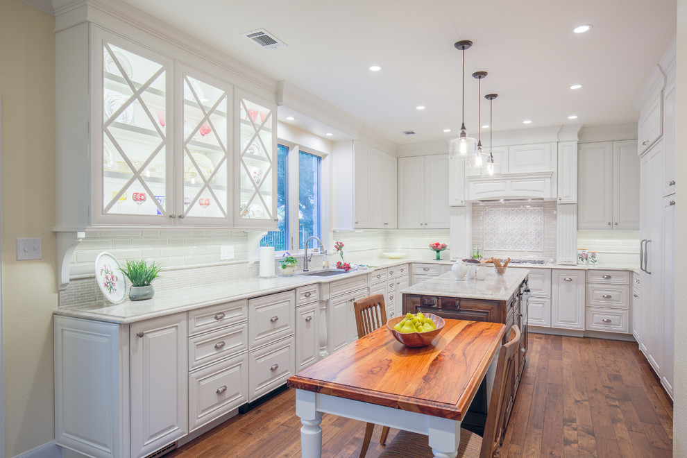 Inspiration for a large country u-shaped eat-in kitchen in Austin with a double-bowl sink, raised-panel cabinets, white cabinets, quartzite benchtops, white splashback, subway tile splashback, panelled appliances, medium hardwood floors and with island.