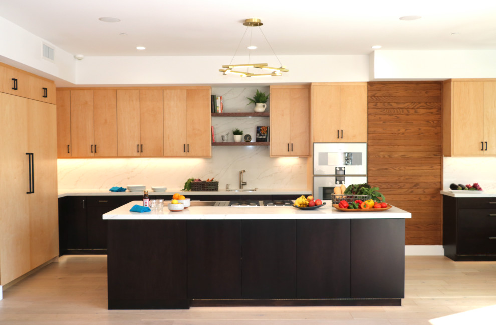 This is an example of a large modern u-shaped open plan kitchen in Los Angeles with an undermount sink, flat-panel cabinets, light wood cabinets, quartz benchtops, white splashback, engineered quartz splashback, stainless steel appliances, medium hardwood floors, with island, white floor and white benchtop.
