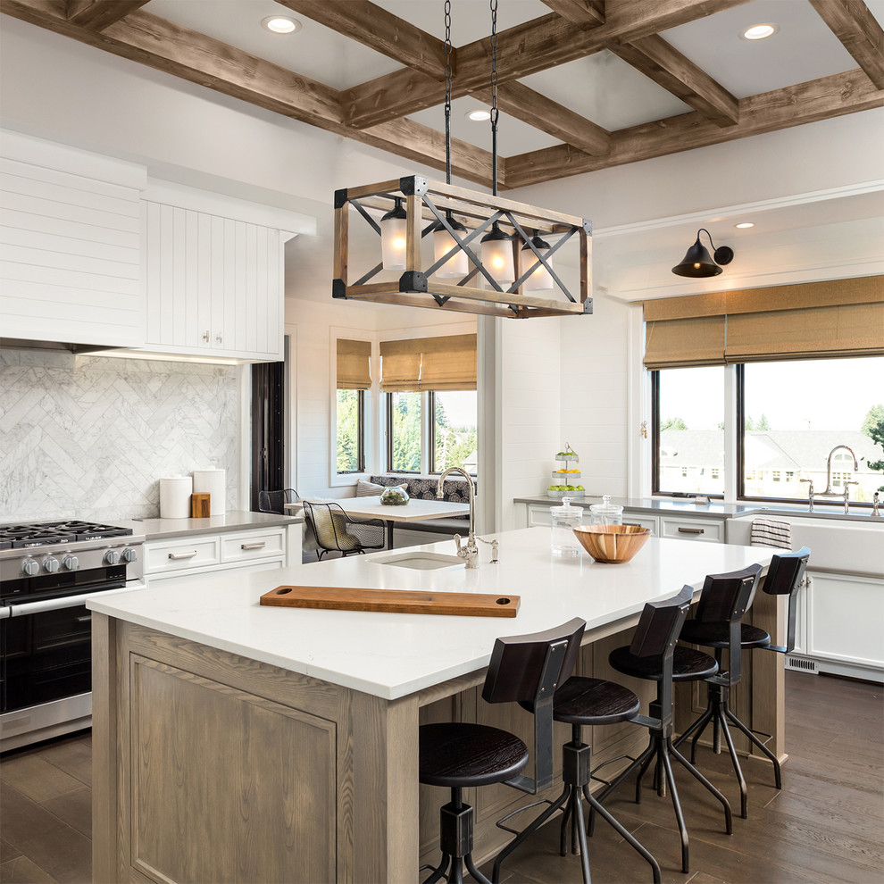 Photo of a country l-shaped eat-in kitchen in Other with a farmhouse sink, recessed-panel cabinets, white cabinets, grey splashback, stainless steel appliances, medium hardwood floors, with island, brown floor and white benchtop.
