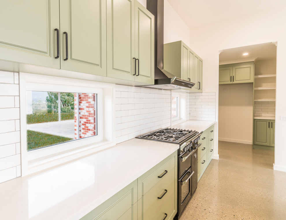 This is an example of a large contemporary galley kitchen pantry in Other with a drop-in sink, recessed-panel cabinets, green cabinets, quartz benchtops, white splashback, ceramic splashback, black appliances, concrete floors, with island, grey floor and white benchtop.