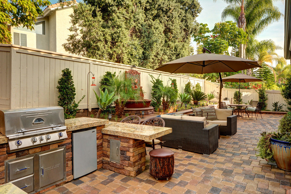 This is an example of a mid-sized mediterranean backyard patio in Orange County with a fire feature, brick pavers and an awning.
