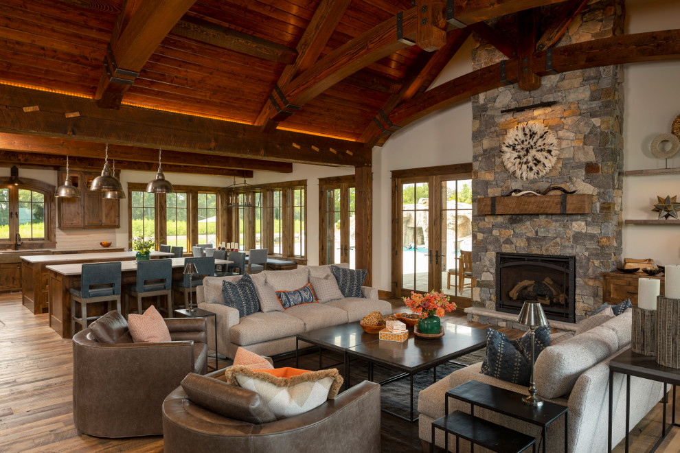 Example of a huge mountain style open concept medium tone wood floor, multicolored floor, exposed beam and shiplap wall family room design in Minneapolis with gray walls, a standard fireplace, a stacked stone fireplace and no tv