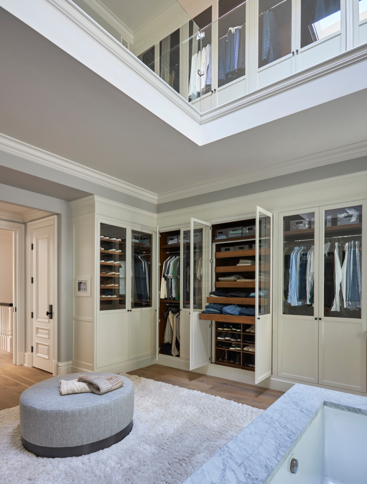 Inspiration for a mid-sized transitional gender-neutral light wood floor, beige floor and vaulted ceiling walk-in closet remodel in Milwaukee with glass-front cabinets and white cabinets
