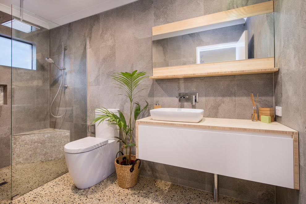 Photo of a mid-sized contemporary bathroom in Other with concrete floors, an open shower, flat-panel cabinets, white cabinets, an alcove shower, gray tile, a vessel sink, wood benchtops, grey floor and beige benchtops.
