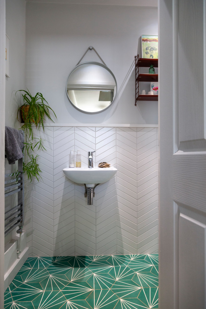 Minimalistisk inredning av ett litet toalett, med vit kakel, porslinskakel, vita väggar, ett väggmonterat handfat och grönt golv