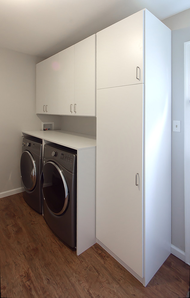 Design ideas for a mid-sized modern galley utility room in Philadelphia with flat-panel cabinets, white cabinets, vinyl floors, a side-by-side washer and dryer, brown floor and grey walls.