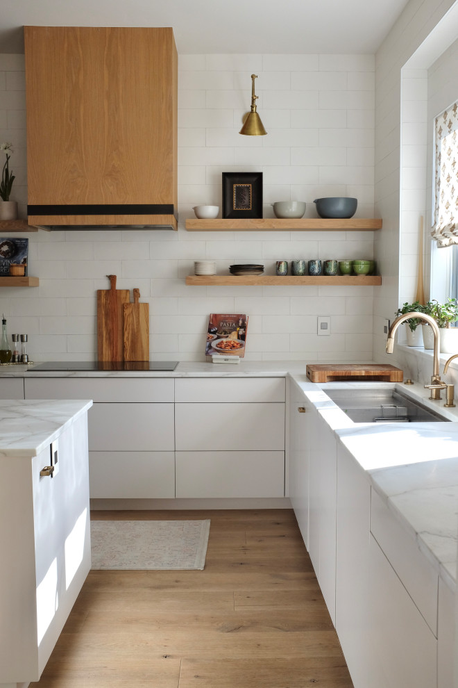 Inspiration for a large contemporary u-shaped kitchen in Denver with a submerged sink, flat-panel cabinets, light wood cabinets, marble worktops, white splashback, metro tiled splashback, light hardwood flooring, an island and white worktops.