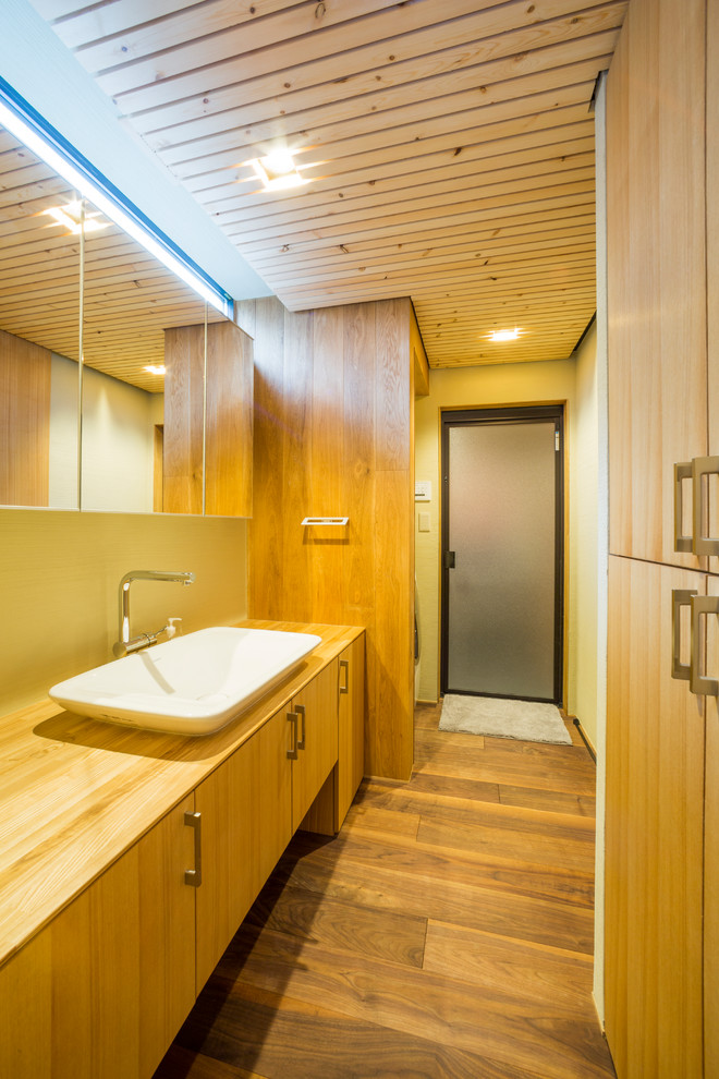This is an example of a modern powder room in Other with flat-panel cabinets, medium wood cabinets, yellow walls, dark hardwood floors, a vessel sink, wood benchtops, brown floor and brown benchtops.