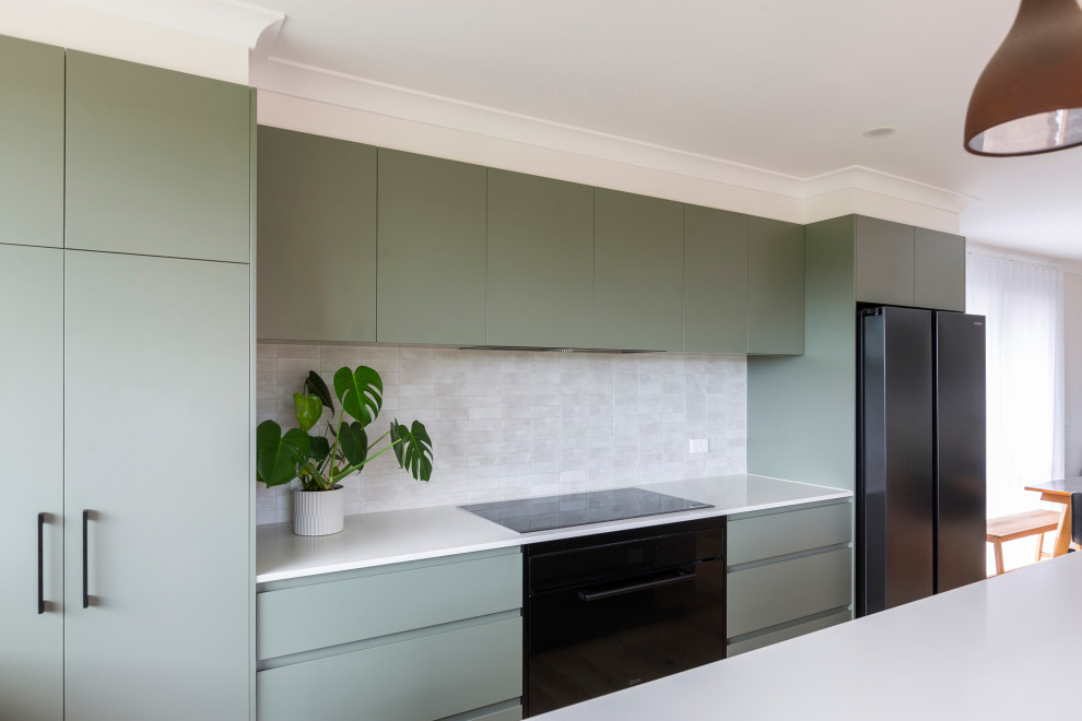 Foto på ett mellanstort funkis grön kök, med en nedsänkt diskho, gröna skåp, bänkskiva i kvarts, vitt stänkskydd, stänkskydd i stenkakel, svarta vitvaror, ljust trägolv, en köksö och beiget golv
