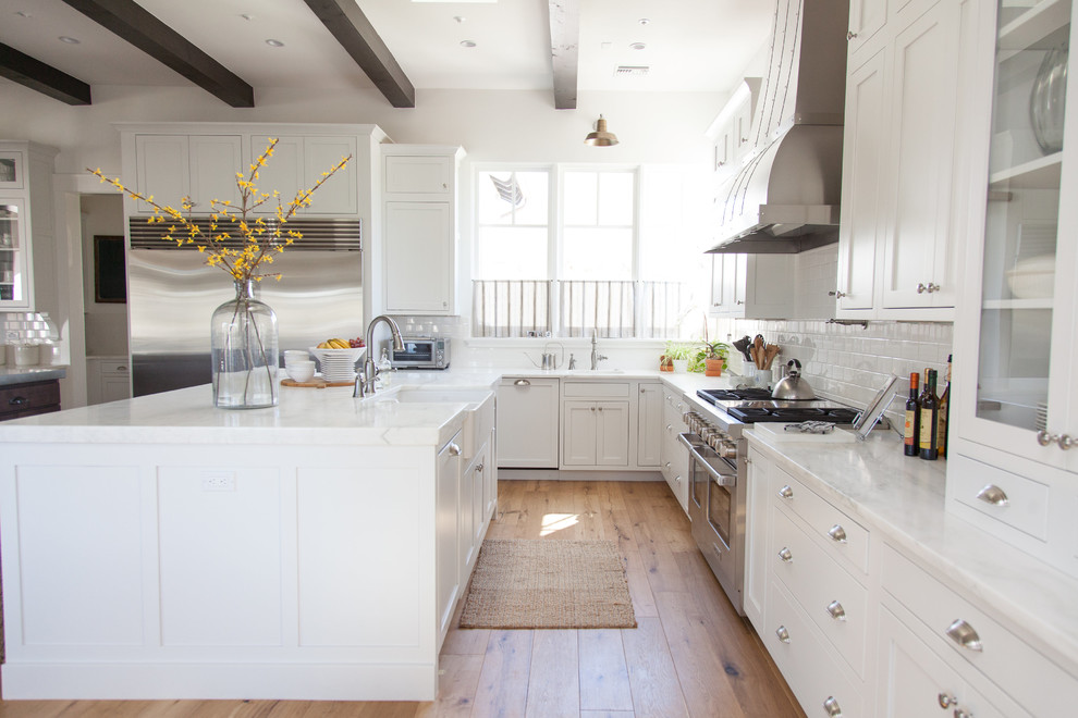 Large transitional l-shaped light wood floor eat-in kitchen photo in Phoenix with a farmhouse sink, white cabinets, white backsplash, stainless steel appliances, an island, stainless steel countertops, shaker cabinets and porcelain backsplash