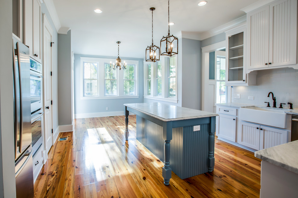 Photo of a mid-sized country u-shaped eat-in kitchen in Charleston with a farmhouse sink, white cabinets, white splashback, subway tile splashback, black appliances, light hardwood floors and with island.