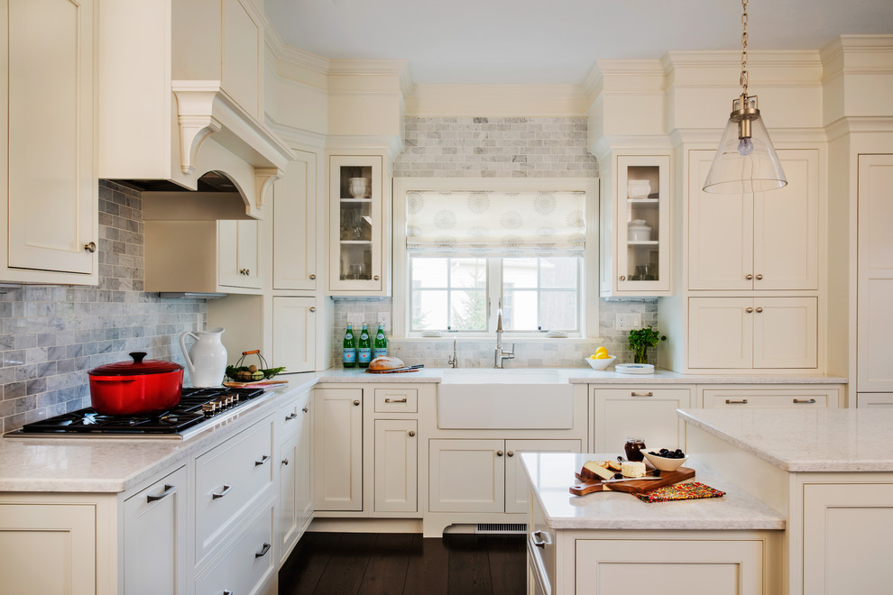 Example of a mid-sized classic l-shaped dark wood floor and brown floor open concept kitchen design in Boston with a farmhouse sink, beaded inset cabinets, white cabinets, marble countertops, gray backsplash, stone tile backsplash, stainless steel appliances and an island