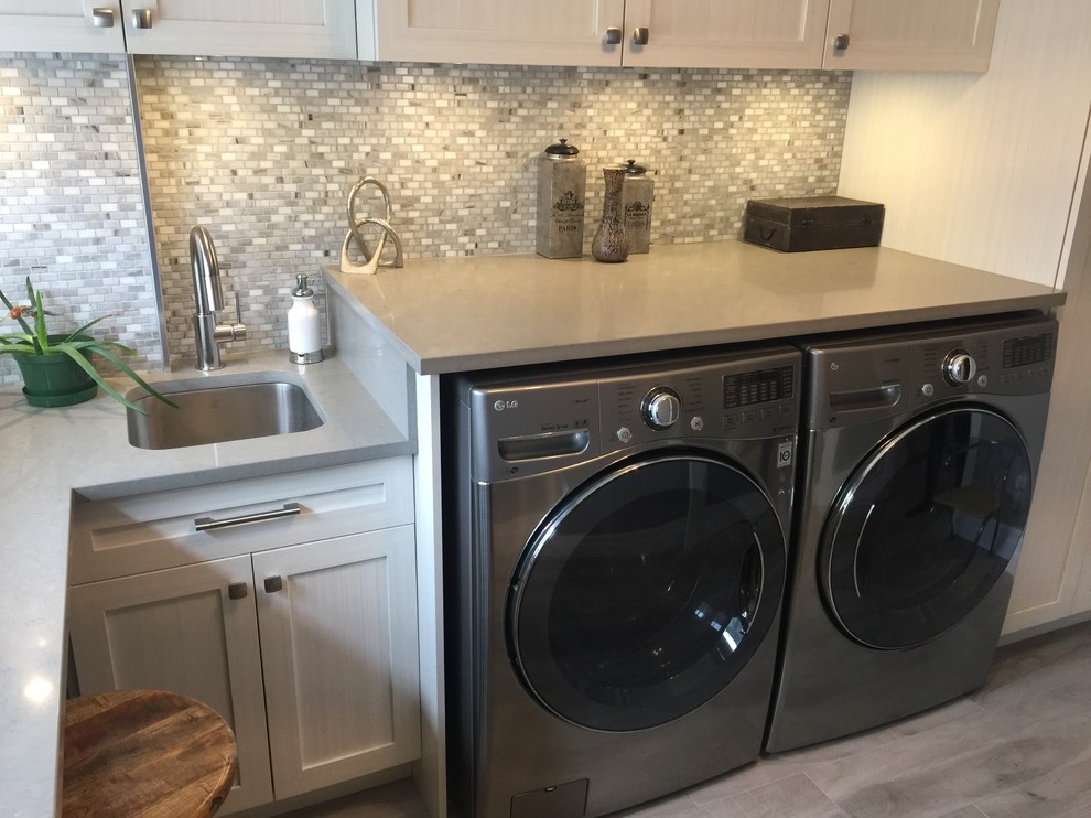 Photo of a mid-sized transitional l-shaped utility room in Montreal with an undermount sink, shaker cabinets, beige cabinets, quartz benchtops, grey walls, porcelain floors, a side-by-side washer and dryer, grey floor and beige benchtop.