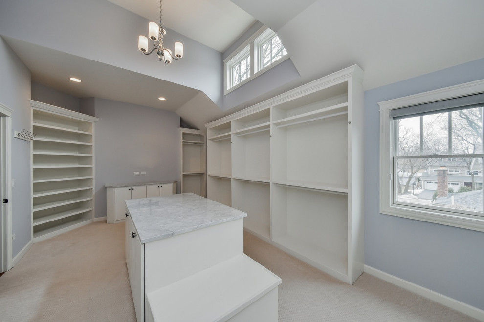 Design ideas for a mid-sized country gender-neutral walk-in wardrobe in Chicago with flat-panel cabinets, white cabinets, carpet, beige floor and vaulted.