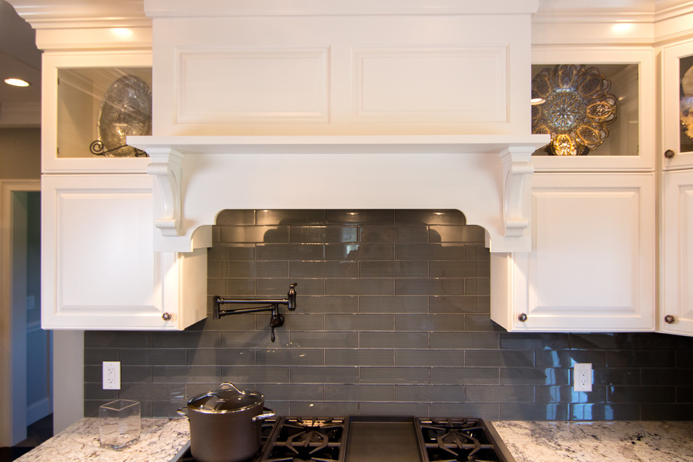 Kitchen - transitional l-shaped dark wood floor kitchen idea in Providence with a farmhouse sink, raised-panel cabinets, granite countertops, gray backsplash, glass tile backsplash, paneled appliances and an island