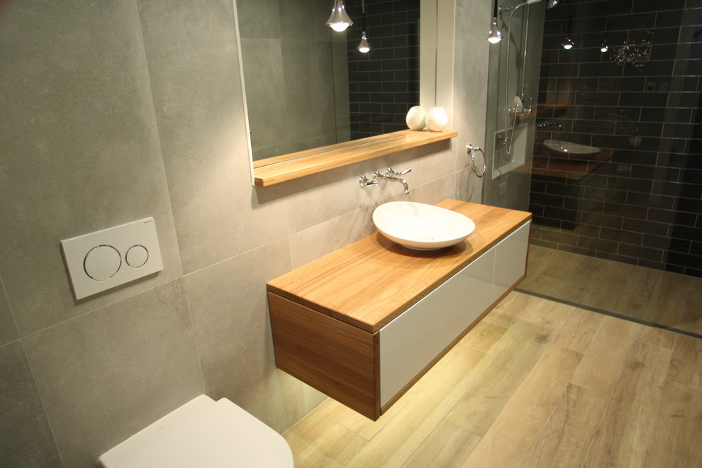 Design ideas for a mid-sized contemporary bathroom in Sydney with furniture-like cabinets, light wood cabinets, an open shower, a one-piece toilet, gray tile, porcelain tile, grey walls, porcelain floors, wood benchtops, grey floor, an open shower and a vessel sink.