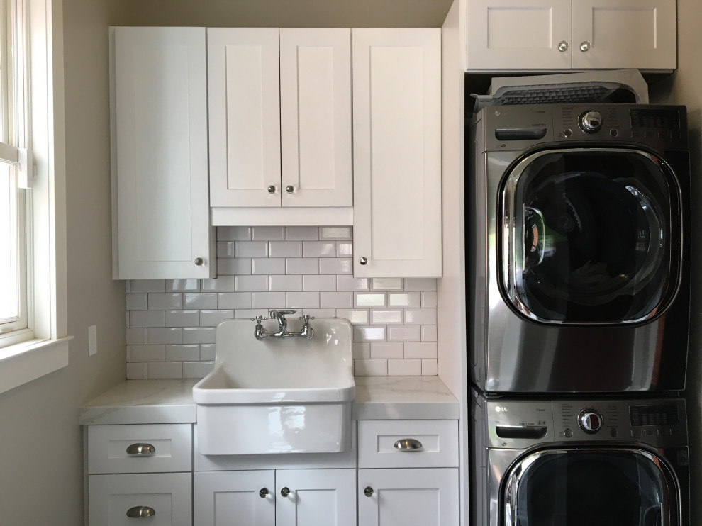 This is an example of a mid-sized arts and crafts single-wall dedicated laundry room in Orlando with a farmhouse sink, shaker cabinets, white cabinets, quartz benchtops, grey walls, porcelain floors, a stacked washer and dryer, grey floor and white benchtop.