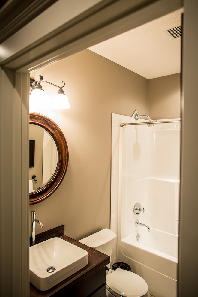 This is an example of a small mediterranean bathroom in Edmonton with shaker cabinets, dark wood cabinets, an alcove tub, a two-piece toilet, brown tile, beige walls, a vessel sink and tile benchtops.