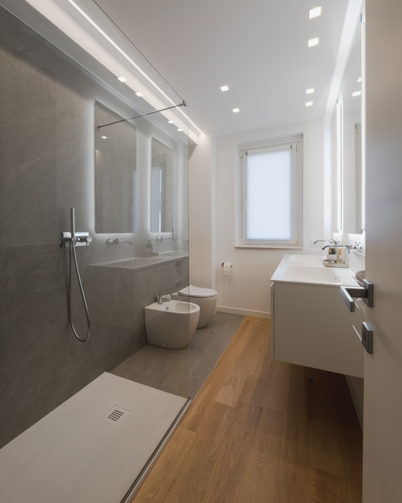 Photo of a mid-sized contemporary 3/4 bathroom in Milan with flat-panel cabinets, white cabinets, an open shower, a two-piece toilet, gray tile, porcelain tile, white walls, light hardwood floors, a drop-in sink, solid surface benchtops, beige floor, white benchtops, a double vanity and a floating vanity.