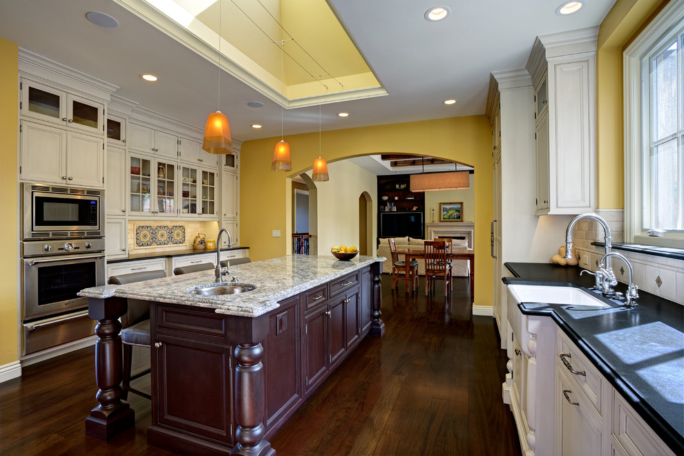 Inspiration for a large transitional u-shaped dark wood floor open concept kitchen remodel in San Francisco with a farmhouse sink, beaded inset cabinets, white cabinets, granite countertops, beige backsplash, stone tile backsplash, paneled appliances and an island