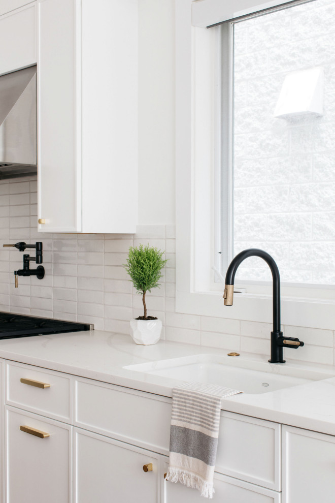 Imagen de cocina moderna con salpicadero blanco, salpicadero de azulejos tipo metro, electrodomésticos de acero inoxidable, suelo de madera oscura y una isla