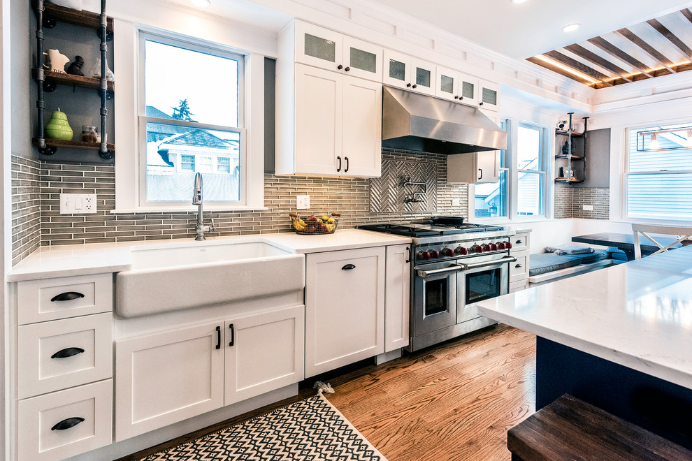 Inspiration for a mid-sized arts and crafts l-shaped eat-in kitchen in Chicago with a farmhouse sink, shaker cabinets, white cabinets, quartzite benchtops, green splashback, glass tile splashback, stainless steel appliances, dark hardwood floors, with island, brown floor and white benchtop.