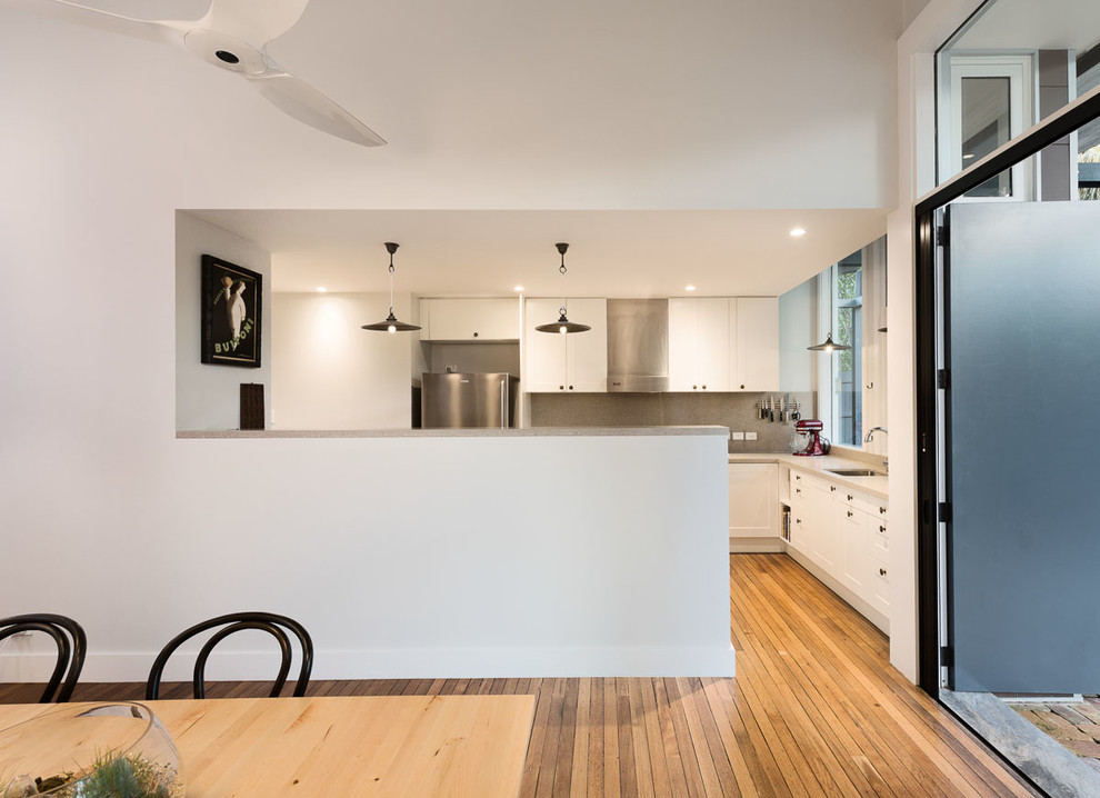 This is an example of a mid-sized contemporary l-shaped separate kitchen in Sydney with an undermount sink, shaker cabinets, white cabinets, concrete benchtops, grey splashback, stone slab splashback, stainless steel appliances, light hardwood floors, with island and beige floor.