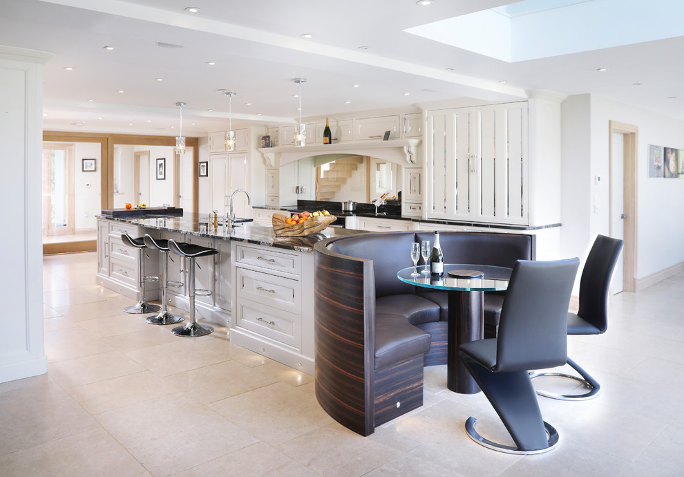 This is an example of a transitional galley eat-in kitchen in Oxfordshire with a farmhouse sink, recessed-panel cabinets, white cabinets, metallic splashback, mirror splashback, panelled appliances, with island, beige floor and black benchtop.