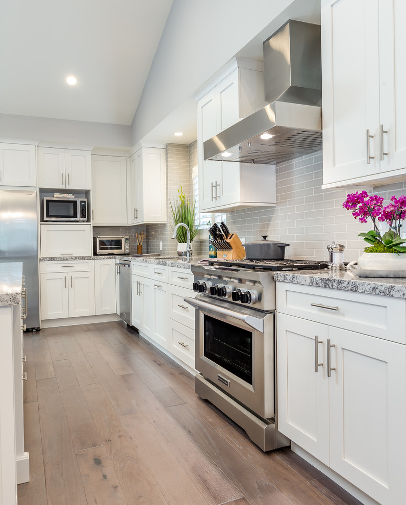Example of a large transitional l-shaped light wood floor eat-in kitchen design in Los Angeles with a single-bowl sink, shaker cabinets, white cabinets, granite countertops, gray backsplash, ceramic backsplash, stainless steel appliances and an island