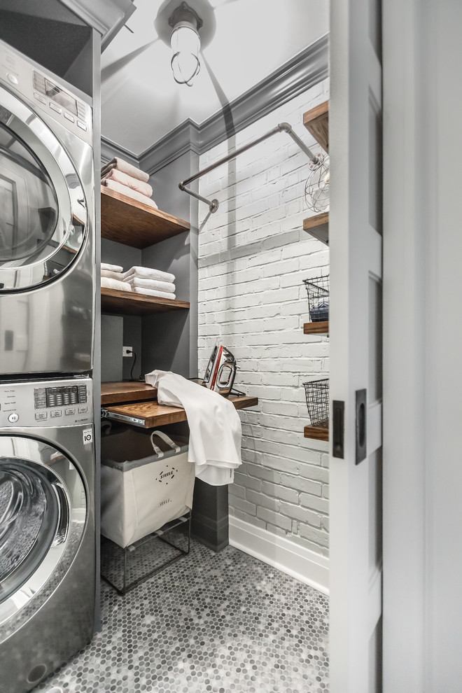 Photo of a small industrial laundry room in Chicago with wood benchtops, grey walls, porcelain floors, a stacked washer and dryer, open cabinets and brown benchtop.