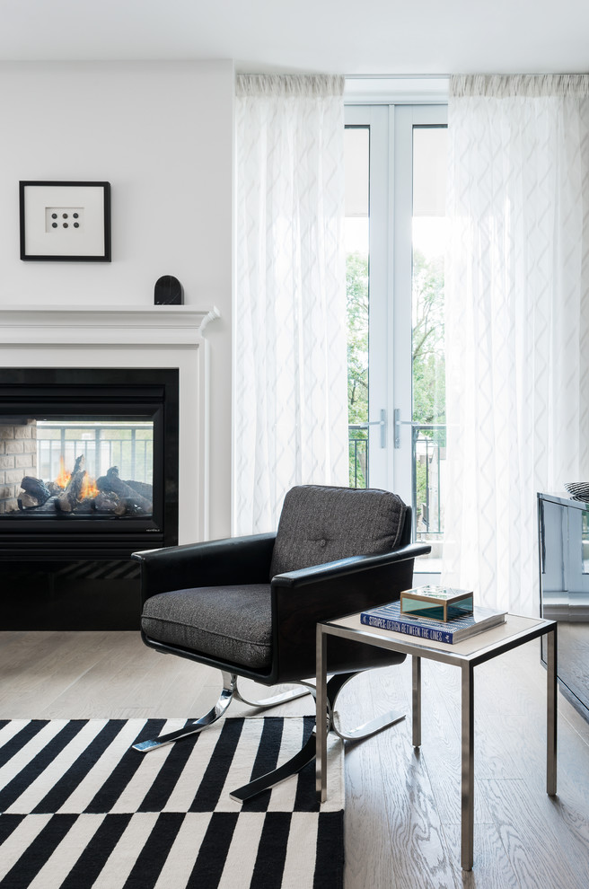 This is an example of a small eclectic open concept living room in Toronto with white walls, light hardwood floors, a two-sided fireplace and a freestanding tv.