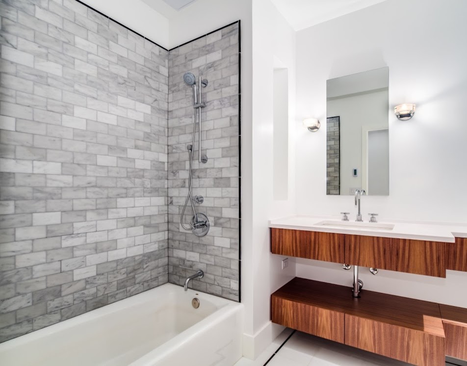 Mid-sized modern bathroom in New York with an undermount sink, furniture-like cabinets, dark wood cabinets, engineered quartz benchtops, an alcove tub, a shower/bathtub combo, a one-piece toilet, gray tile, stone tile, white walls and marble floors.